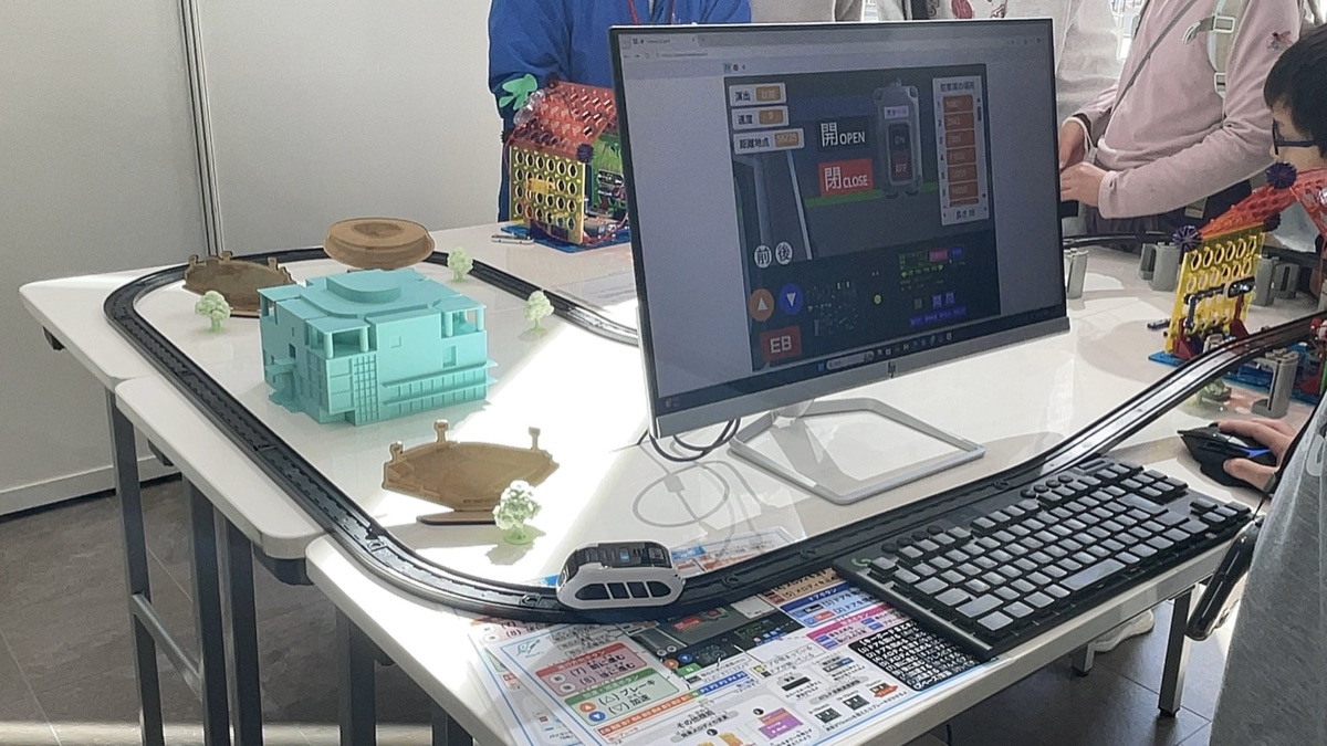 日本語で制作されたScratchの運転画面と、線路を走るスマートトレイン